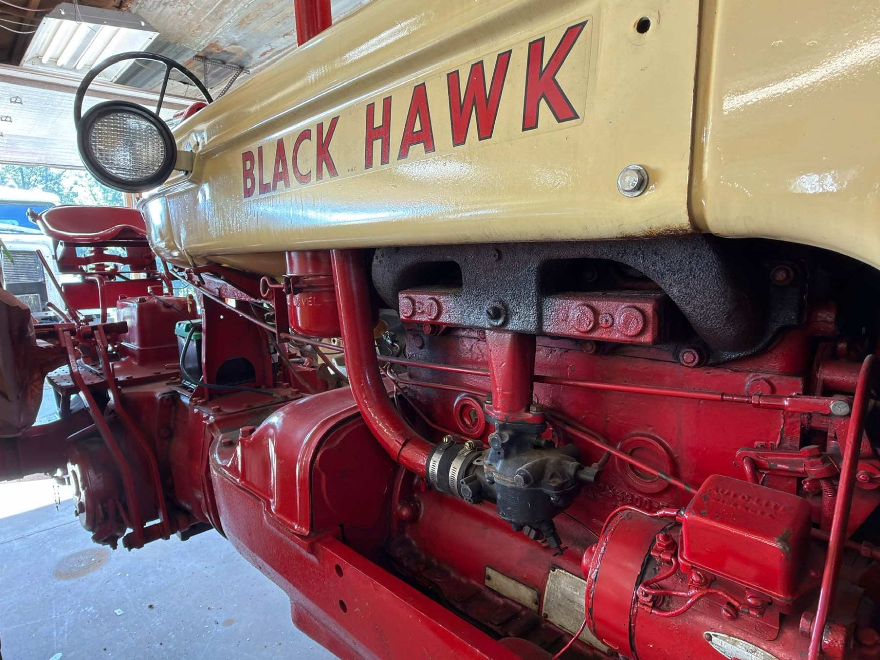 Restored red and cream Black Hawk tractor in the shop, engine side view